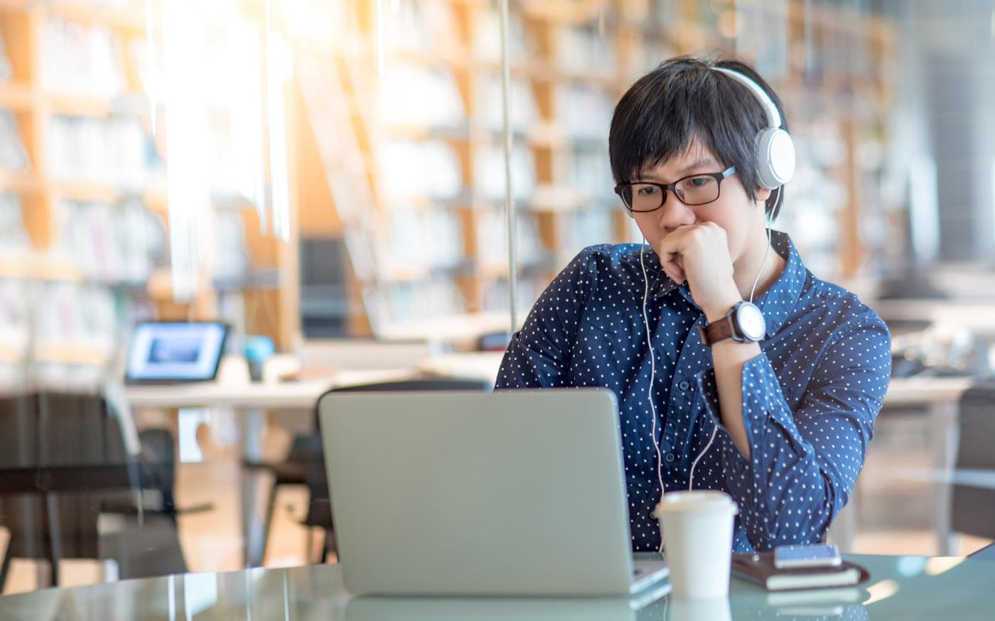 Person sitting at table with headphones on, typing on computer.